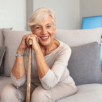 A smiling older woman sitting on a couch while holding a cane