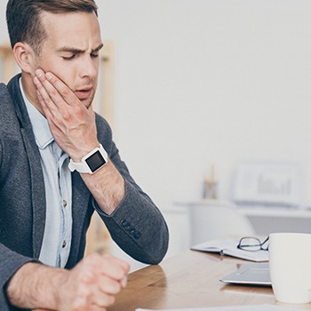 Man sitting at laptop rubbing jaw in pain