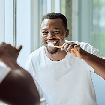 Man brushing teeth in bathroom mirror
